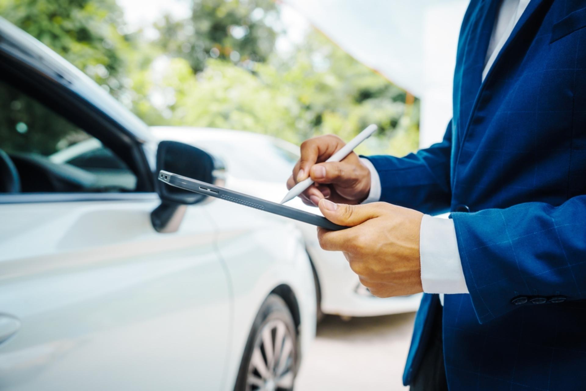 A man reviews a tablet while standing next to two vehicles